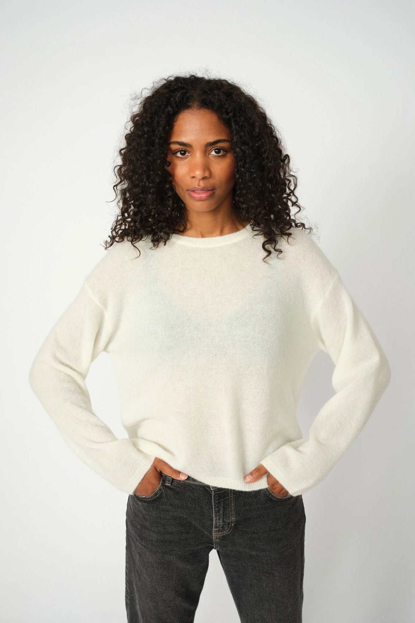 Person wearing a white sweater and dark jeans on a plain background