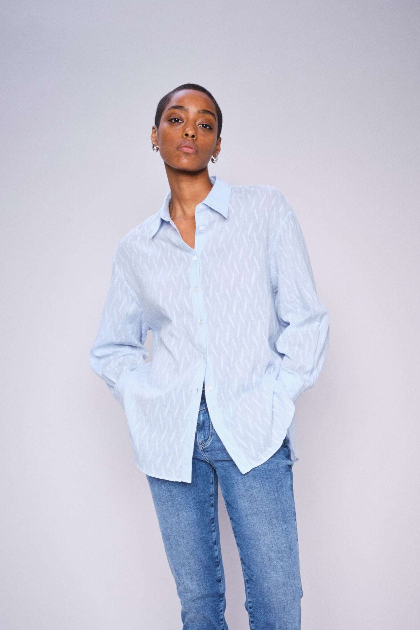 Person wearing a light blue shirt and  mid blue slim leg jeans against a plain background