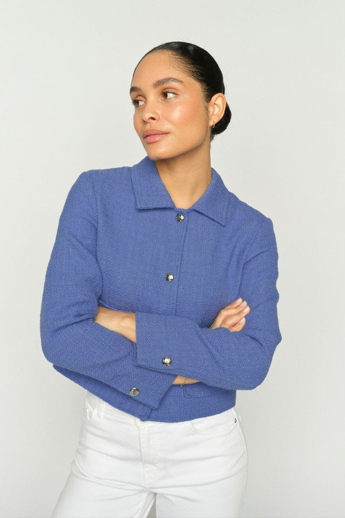 Women wearing a blue textured blazer with white pants on a clean white background.