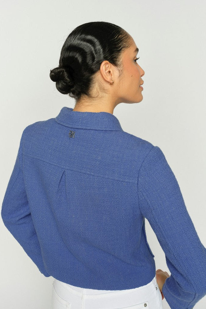 Women wearing a blue textured blazer with white pants on a clean white background.