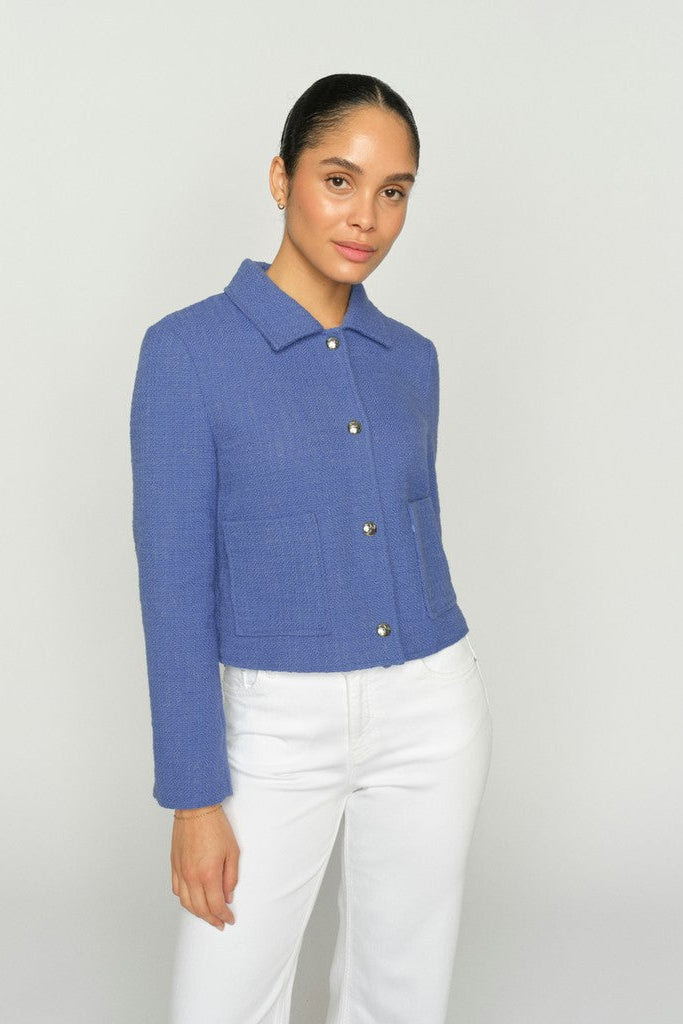 Women wearing a blue textured blazer with white pants on a clean white background.