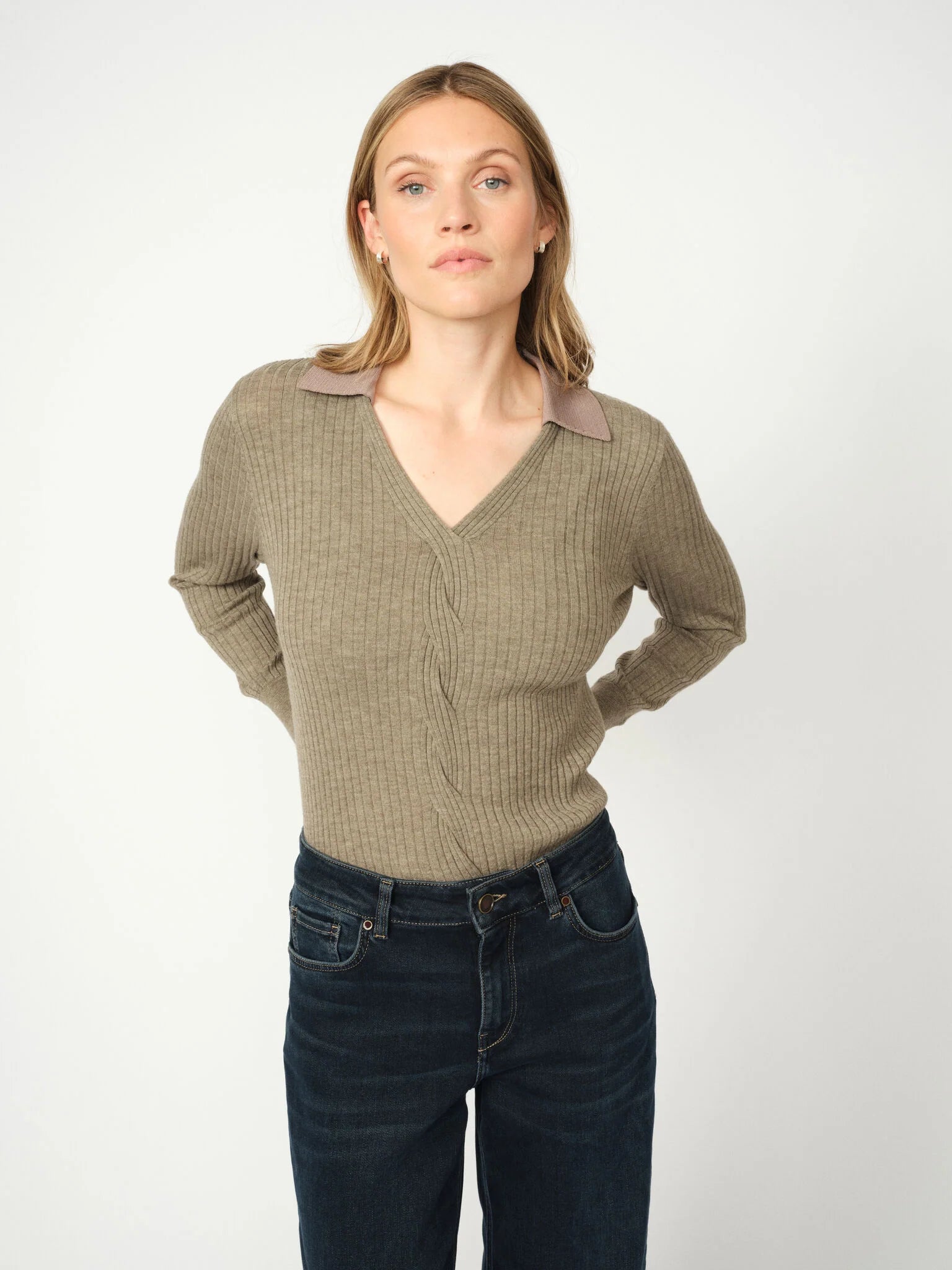Woman wearing a brown polo sweater with a collar and dark jeans on a white background