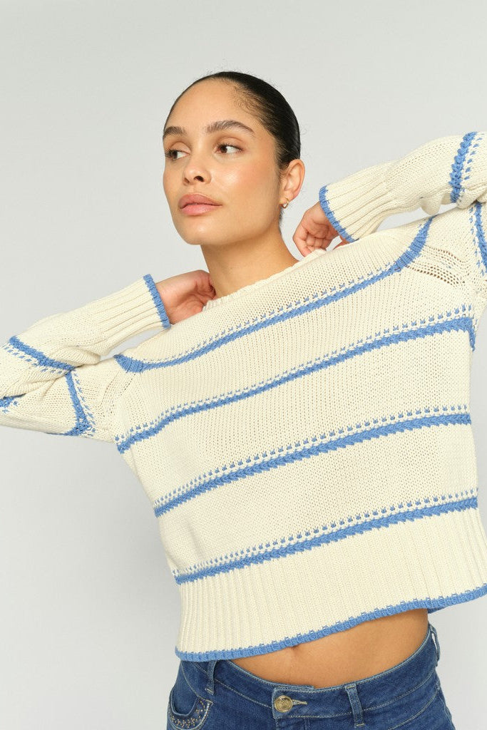 Woman  wearing a shite sweater with blue stripes and blue denim jeans on a white background
