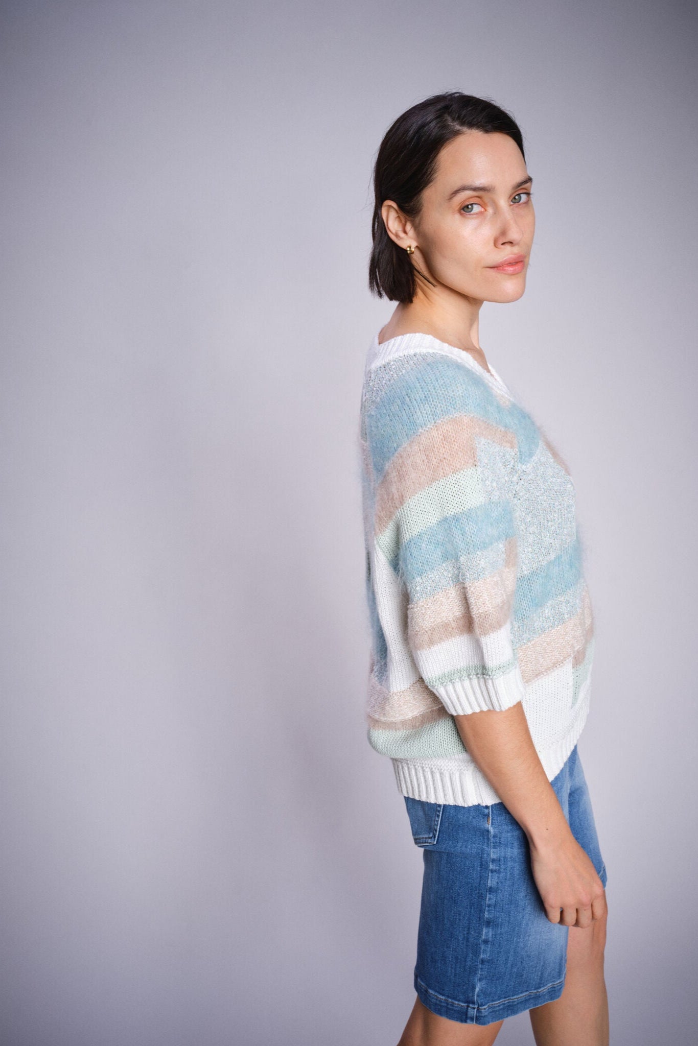 Woman wearing a colorful sweater and denim shorts against a gray background