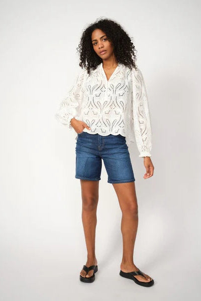 Woman wearing a white embroidered blouse and blue denim shorts on a white background