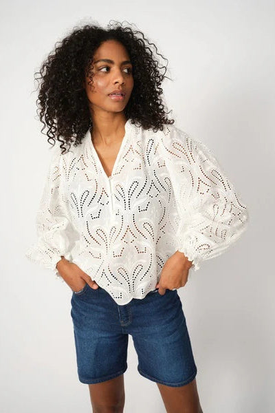 Woman wearing a white embroidered blouse and blue denim shorts on a white background