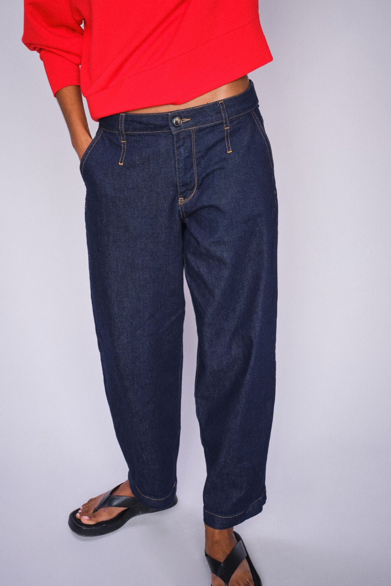 Person wearing blue chino style jeans and a red top on a plain background