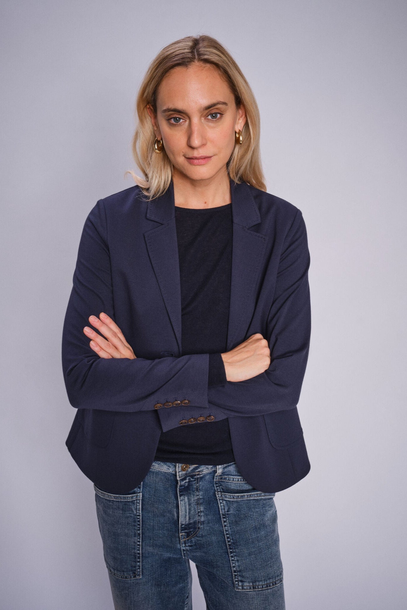 Woman wearing a navy blazer and jeans against a gray background