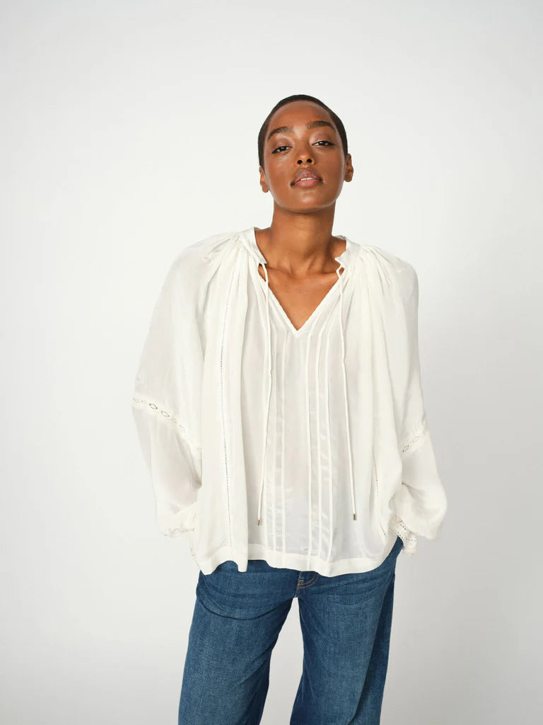Woman wearing ecru long sleeve blouse with lace detailing and blue denim jeans on a white background