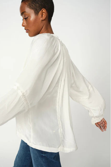 Woman wearing ecru long sleeve blouse with lace detailing and blue denim jeans on a white background