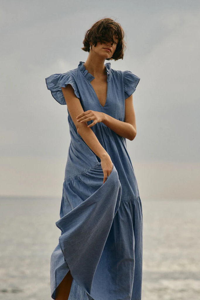 Woman wearing a blue dress with ruffle sleeve standing by a body of water 
