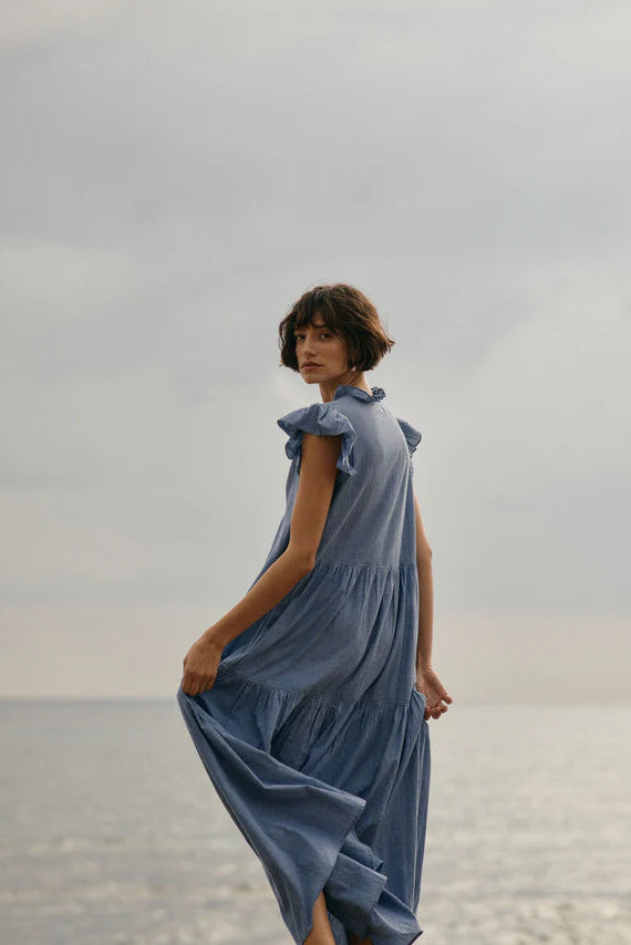 Woman wearing a blue dress with ruffle sleeve standing by a body of water 