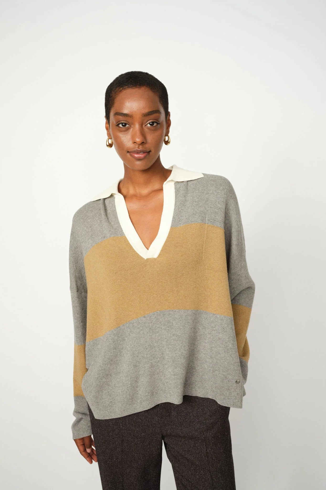 Woman wearing a color-blocked sweater with gray, beige, and white sections on a plain background
