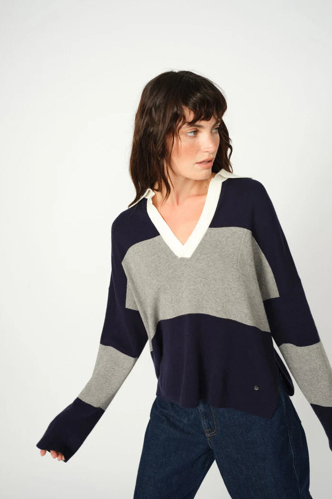 Woman wearing a color-blocked sweater with navy, gray, and white sections on a plain background.