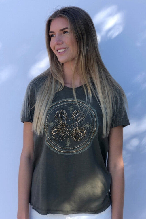 Woman wearing a dark green t-shirt with a circular design against a light blue background