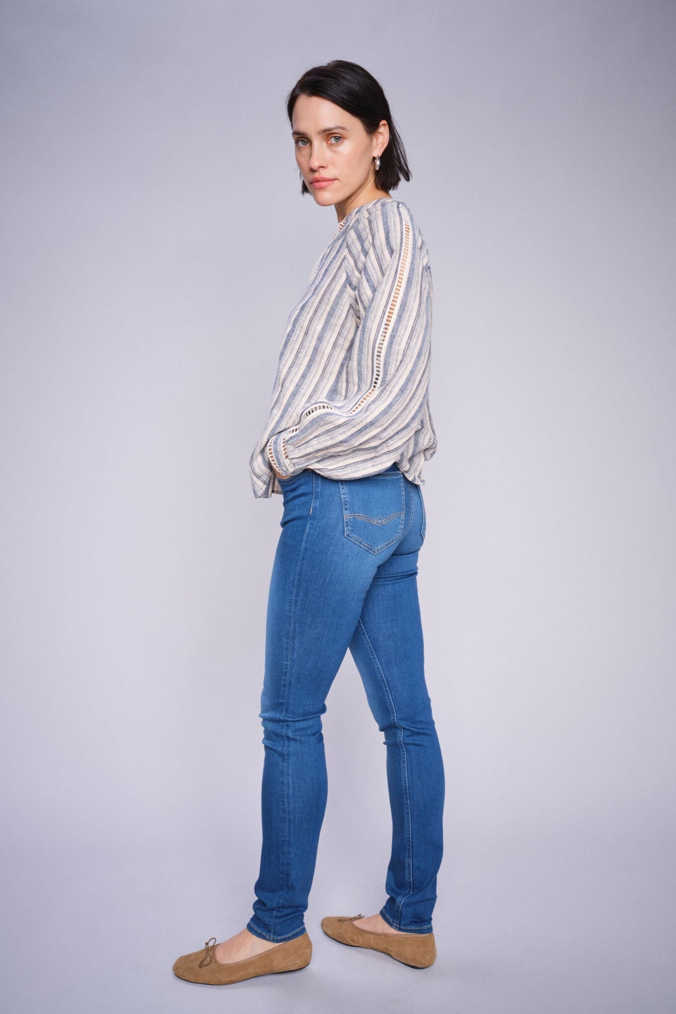 Woman wearing a linen cotton striped shirt and blue jeans on a gray background