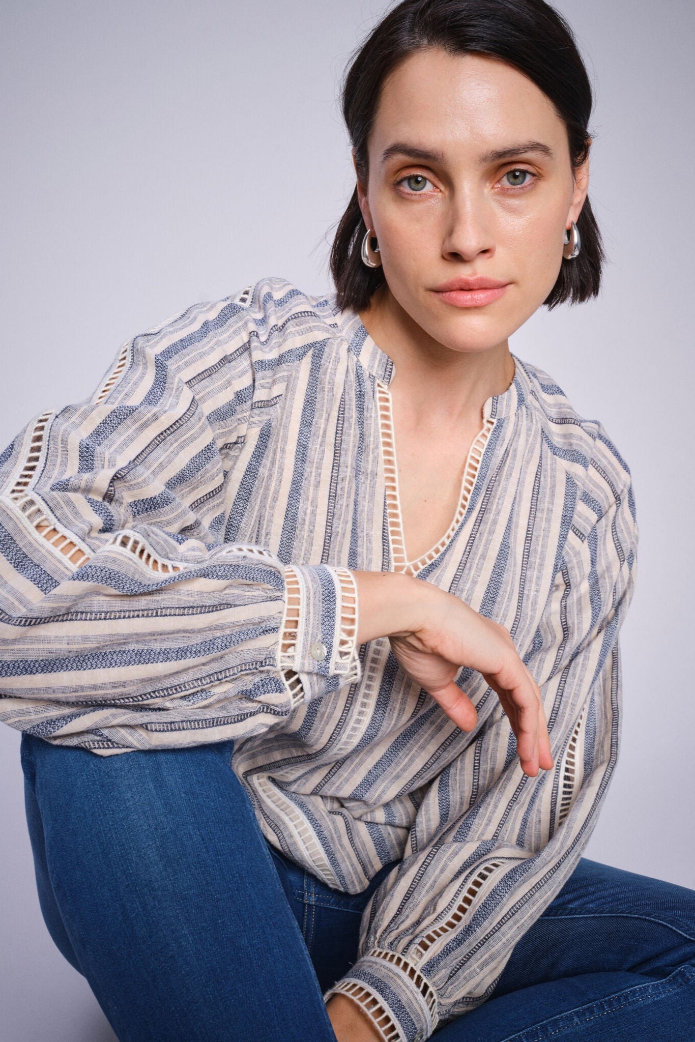 Woman wearing a blue and white stripe cotton linen blouse and blue jeans against a plain background