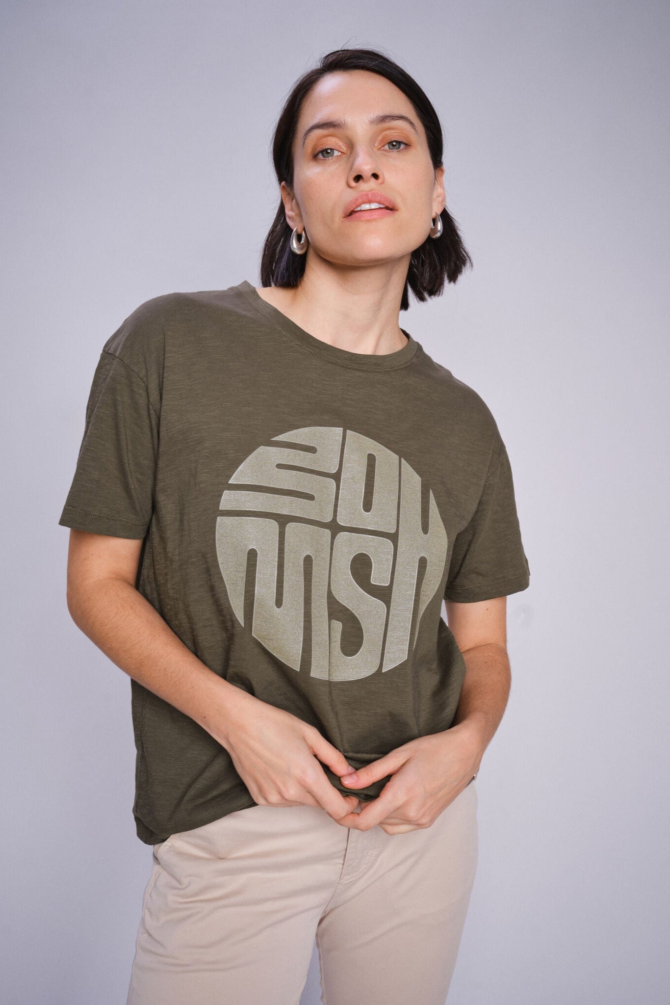 Model  wearing a olive green t-shirt with a logo on a plain background