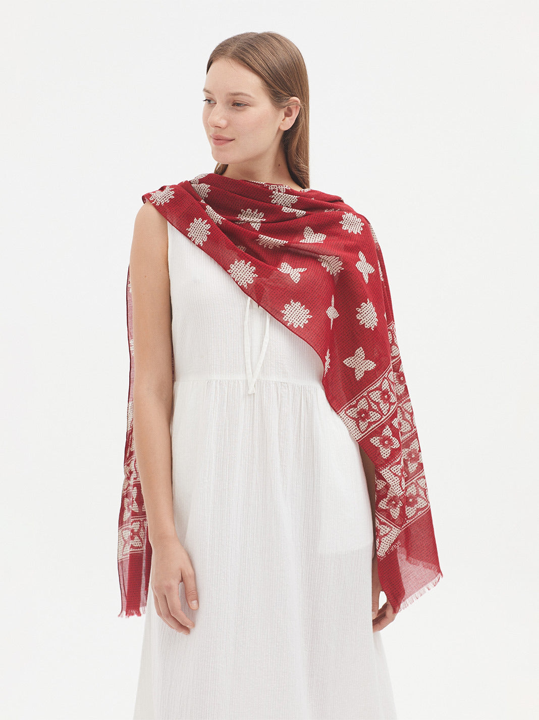 Model wearing white dress with long scarf with red base and all over white floral print. 