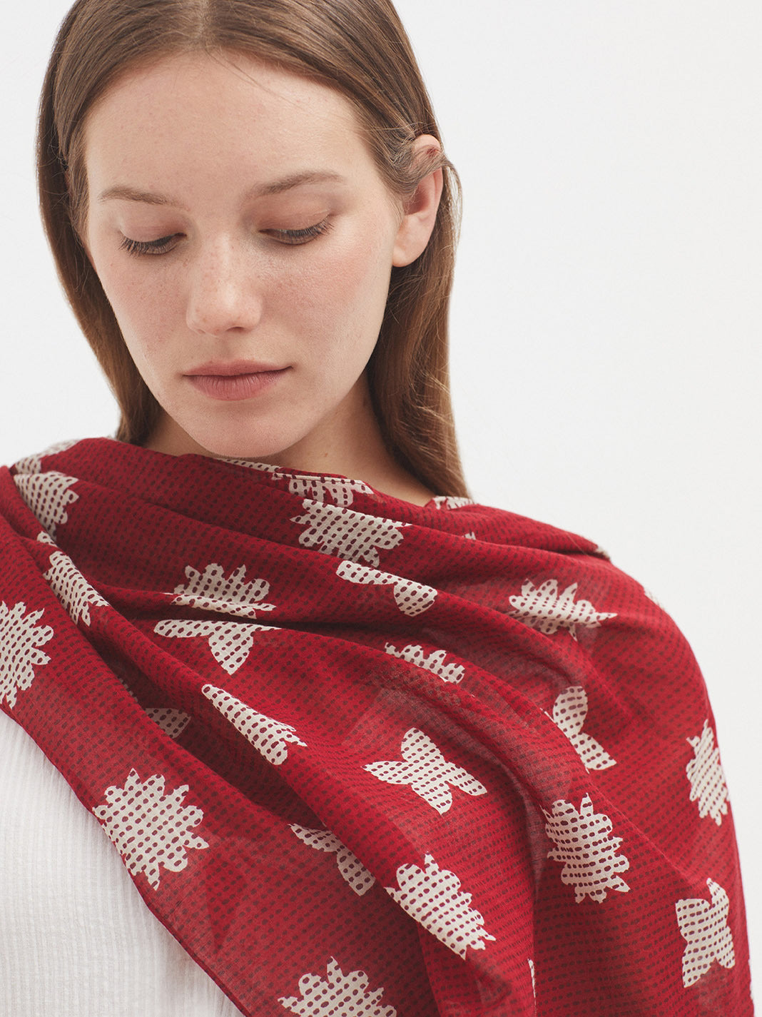 Model wearing white dress with long scarf with red base and all over white floral print. 