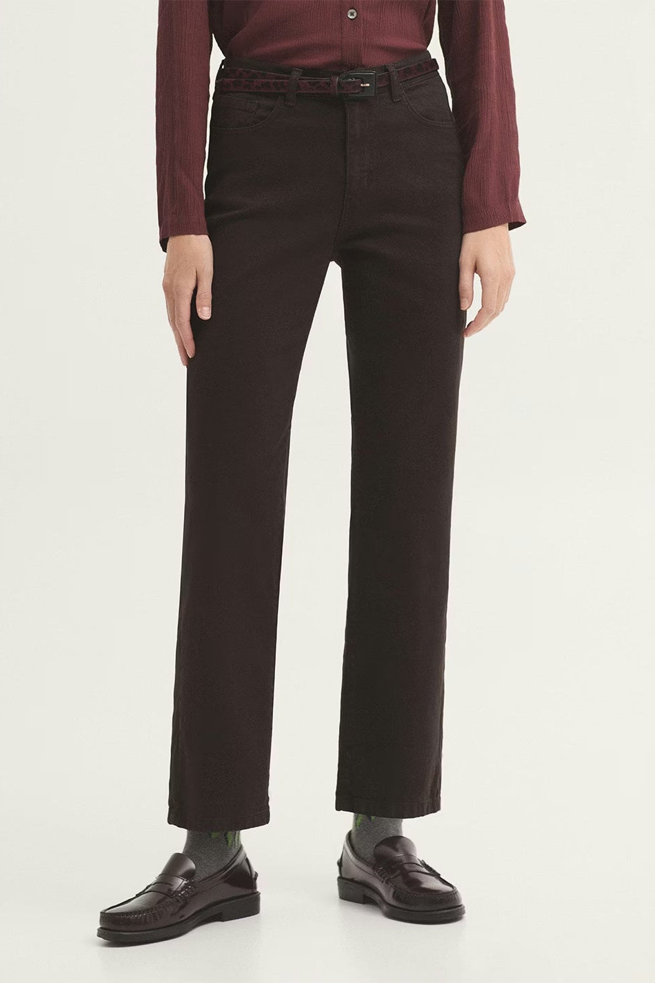 Person wearing dark brown pants and a red top on a white background with black loafers