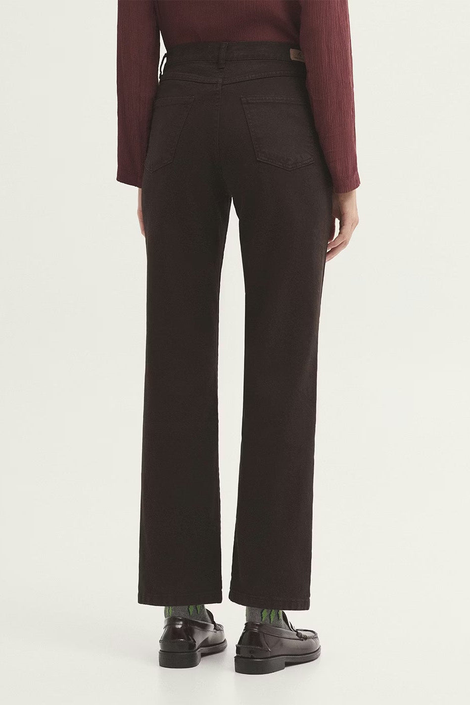 Person wearing dark brown pants and a red top on a white background with black loafers