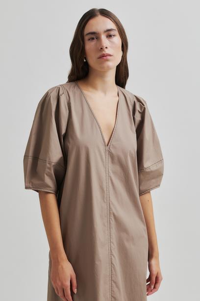 Woman wearing a beige Maxi dress with contrast stitching and short sleeves against a plain background