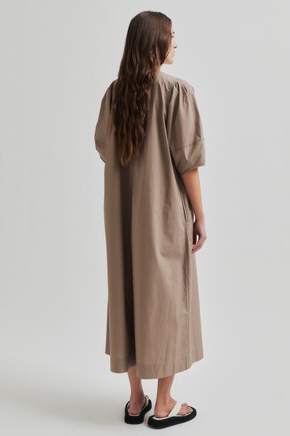 Woman wearing a beige Maxi dress with contrast stitching and short sleeves against a plain background