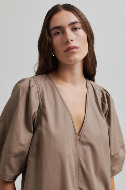 Woman wearing a beige Maxi dress with contrast stitching and short sleeves against a plain background