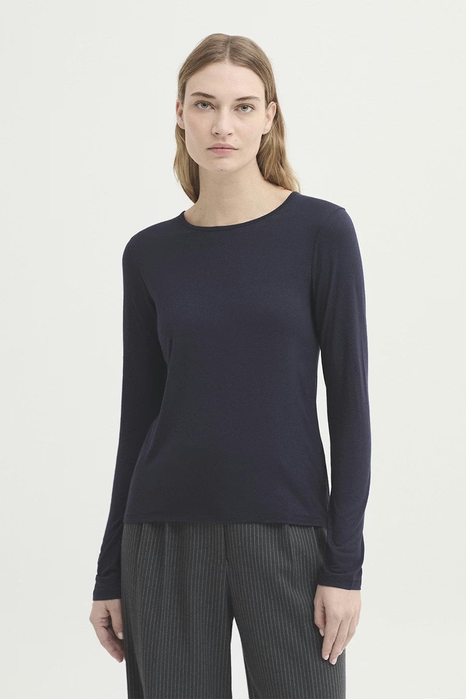 Womanwearing a navy long-sleeve top and gray pants on a white background