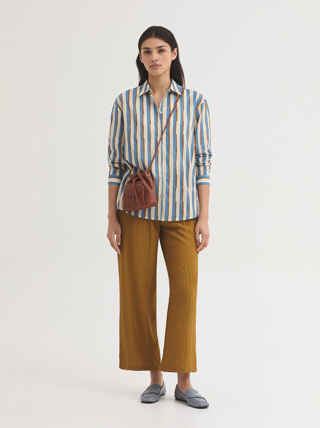 Woman wearing a striped shirt and brown pants with a brown bag on a white background