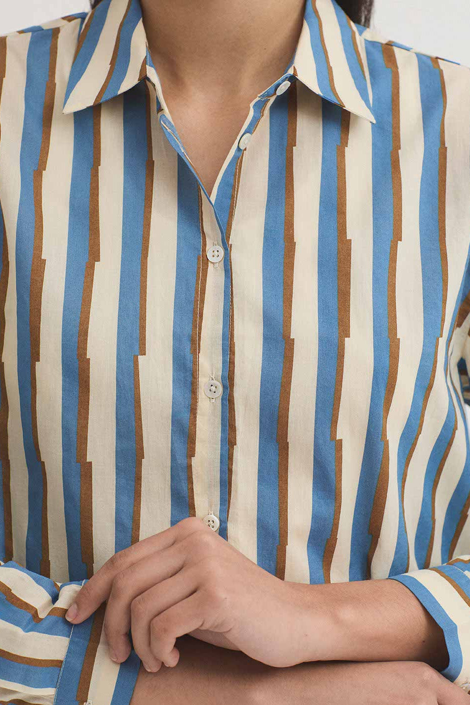 A close-up of a person wearing a long-sleeve button-up shirt with vertical stripes in blue, brown, and cream.