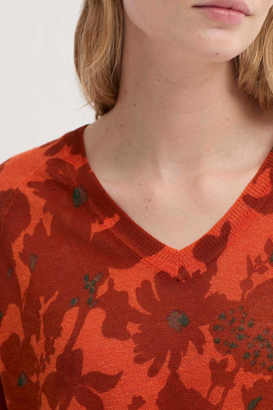 Close-up of a model wearing a vibrant orange-red V-neck knit sweater with a dark floral pattern.