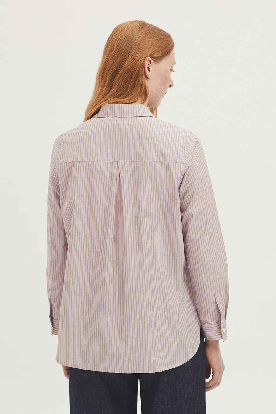 Woman wearing a striped shirt from behind on a light background