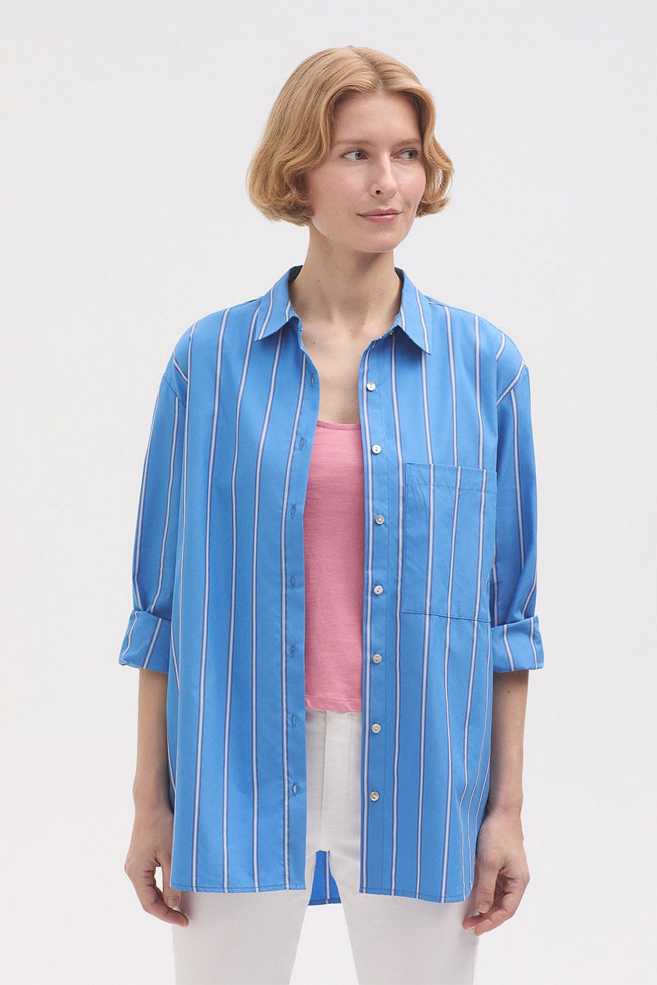 Model wearing a blue striped shirt over a pink top with white trousers. 