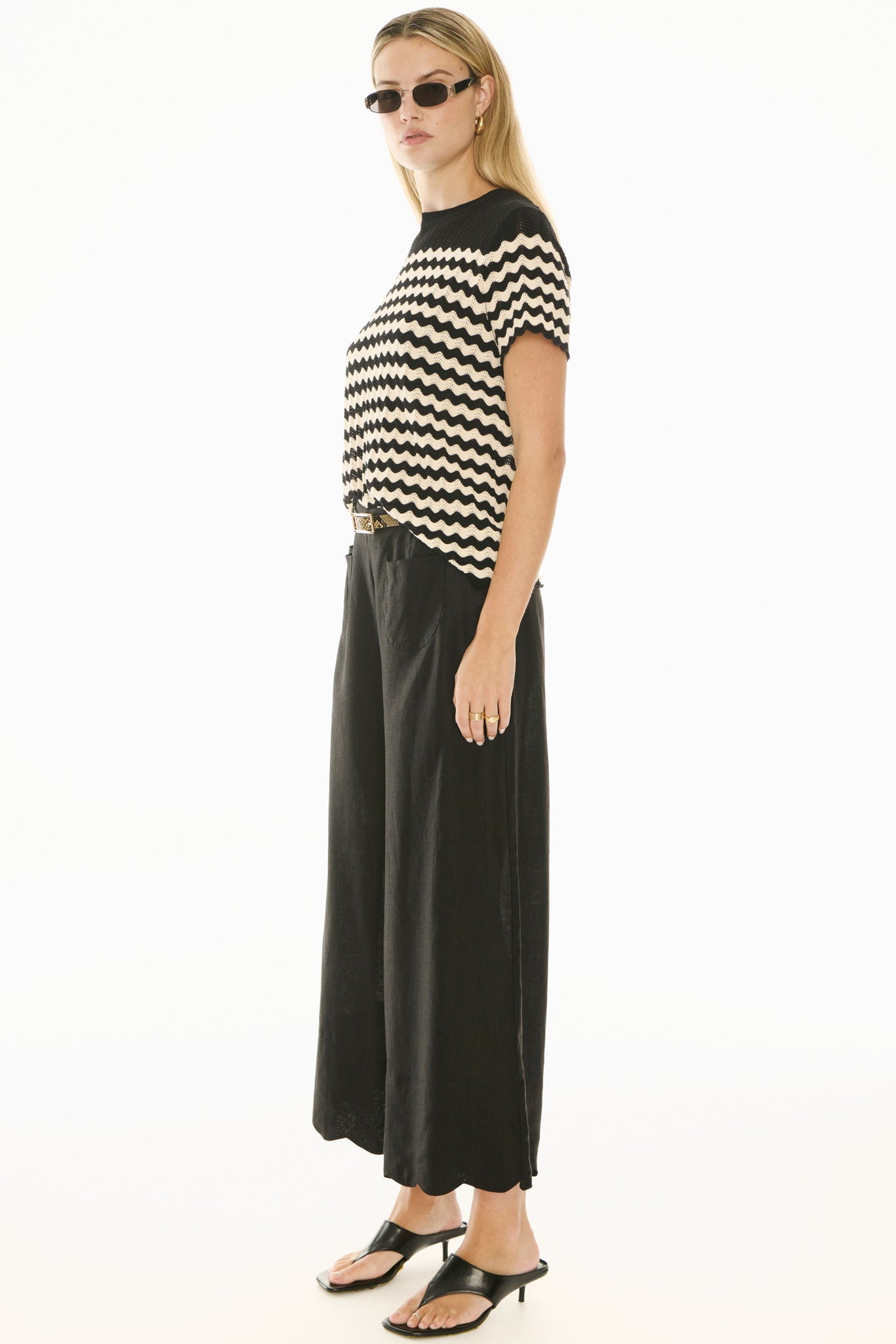 Woman wearing black and white knit short sleeve top and black pants on white background. 