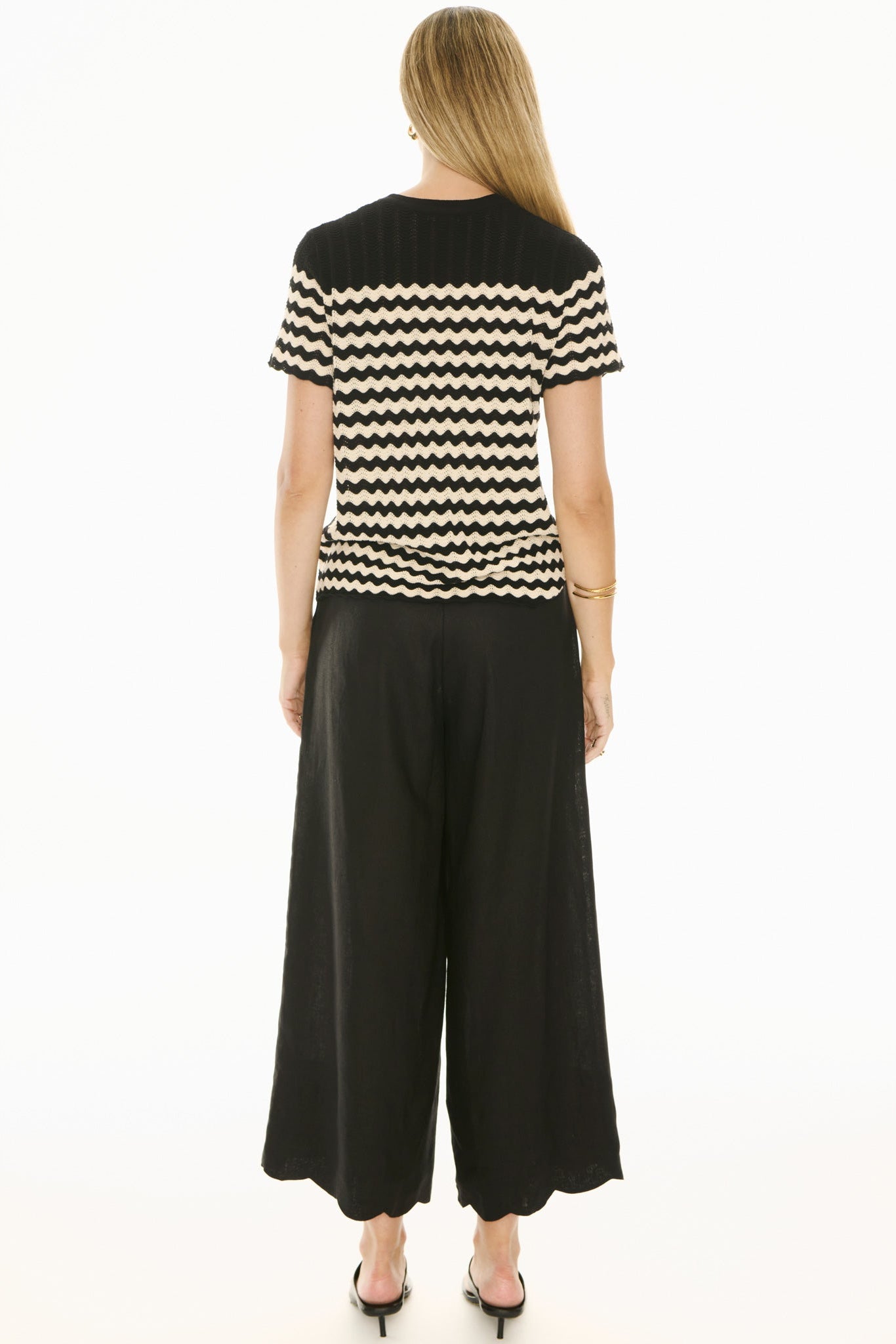 Woman wearing black and white knit short sleeve top and black pants on white background. 