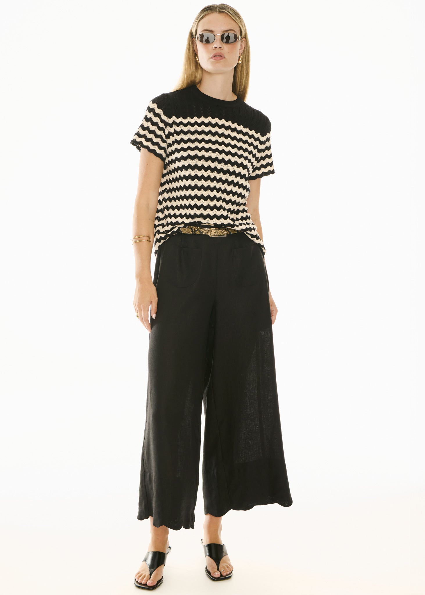 Woman wearing black and white knit short sleeve top and black pants on white background. 