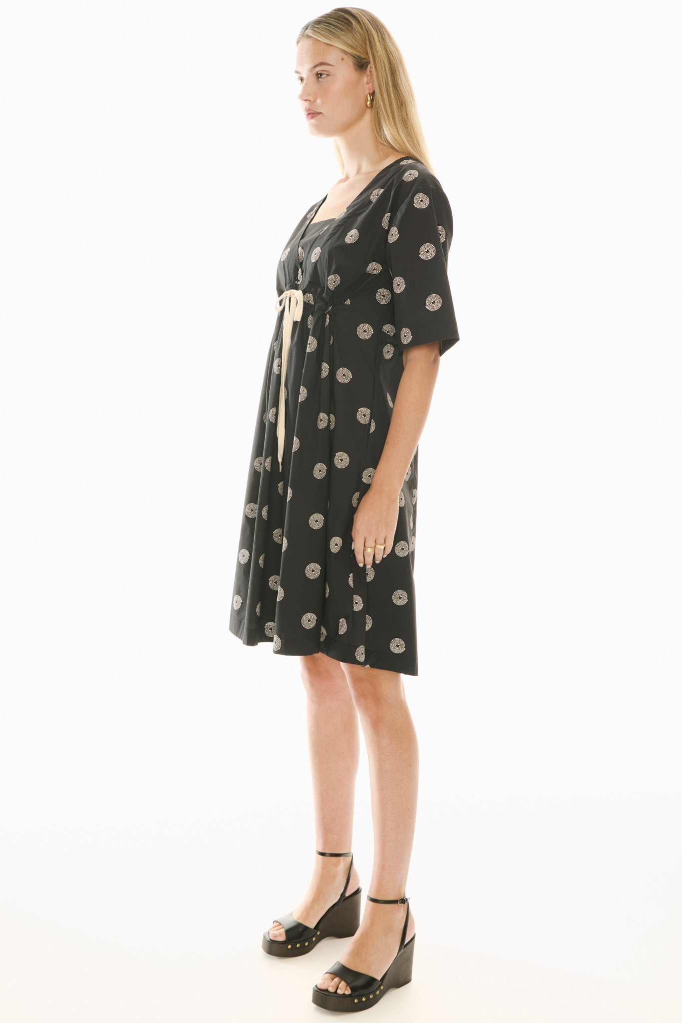 Woman wearing a short sleeve black dress with beige pattern on a white background
