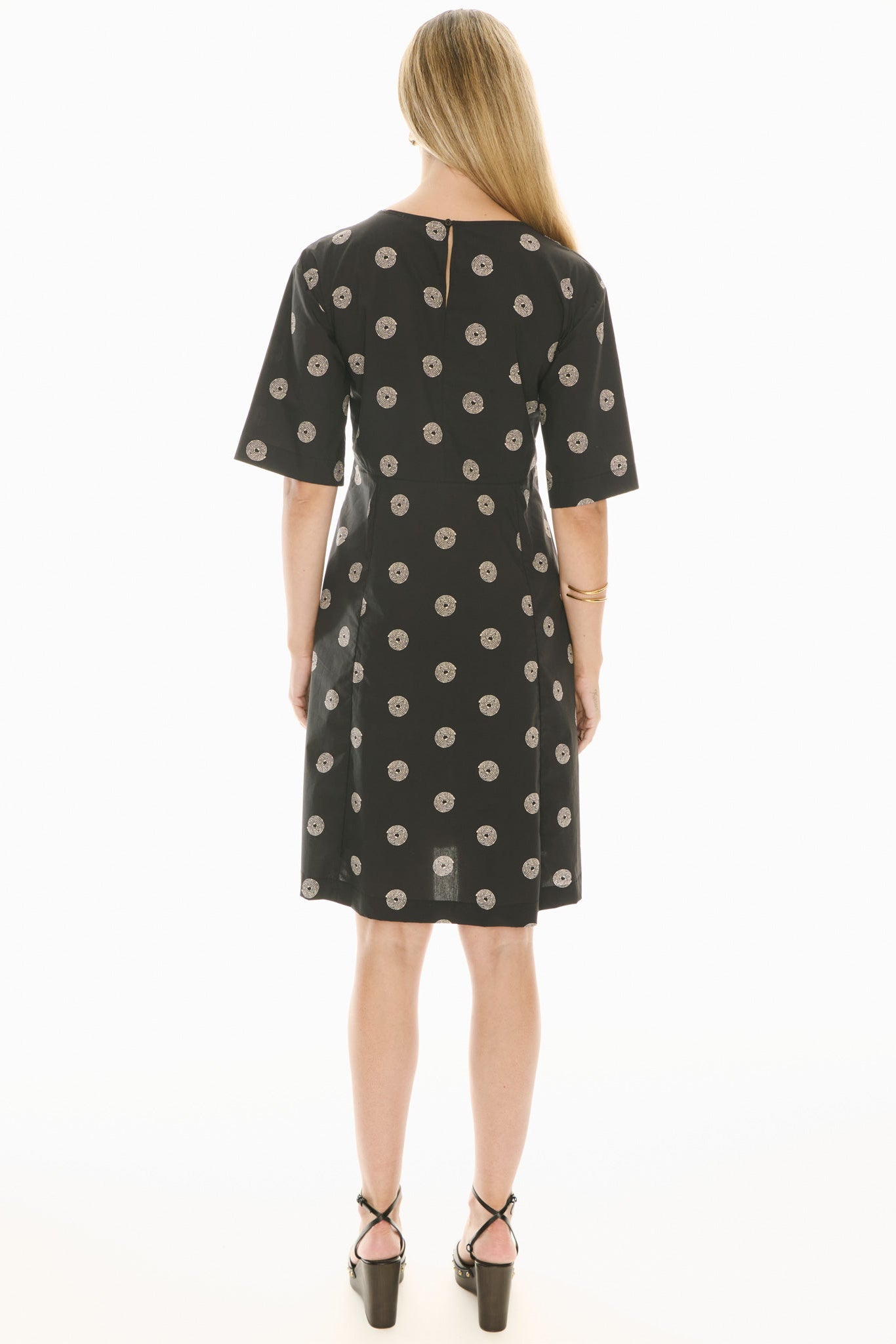 Woman wearing a short sleeve black dress with beige pattern on a white background