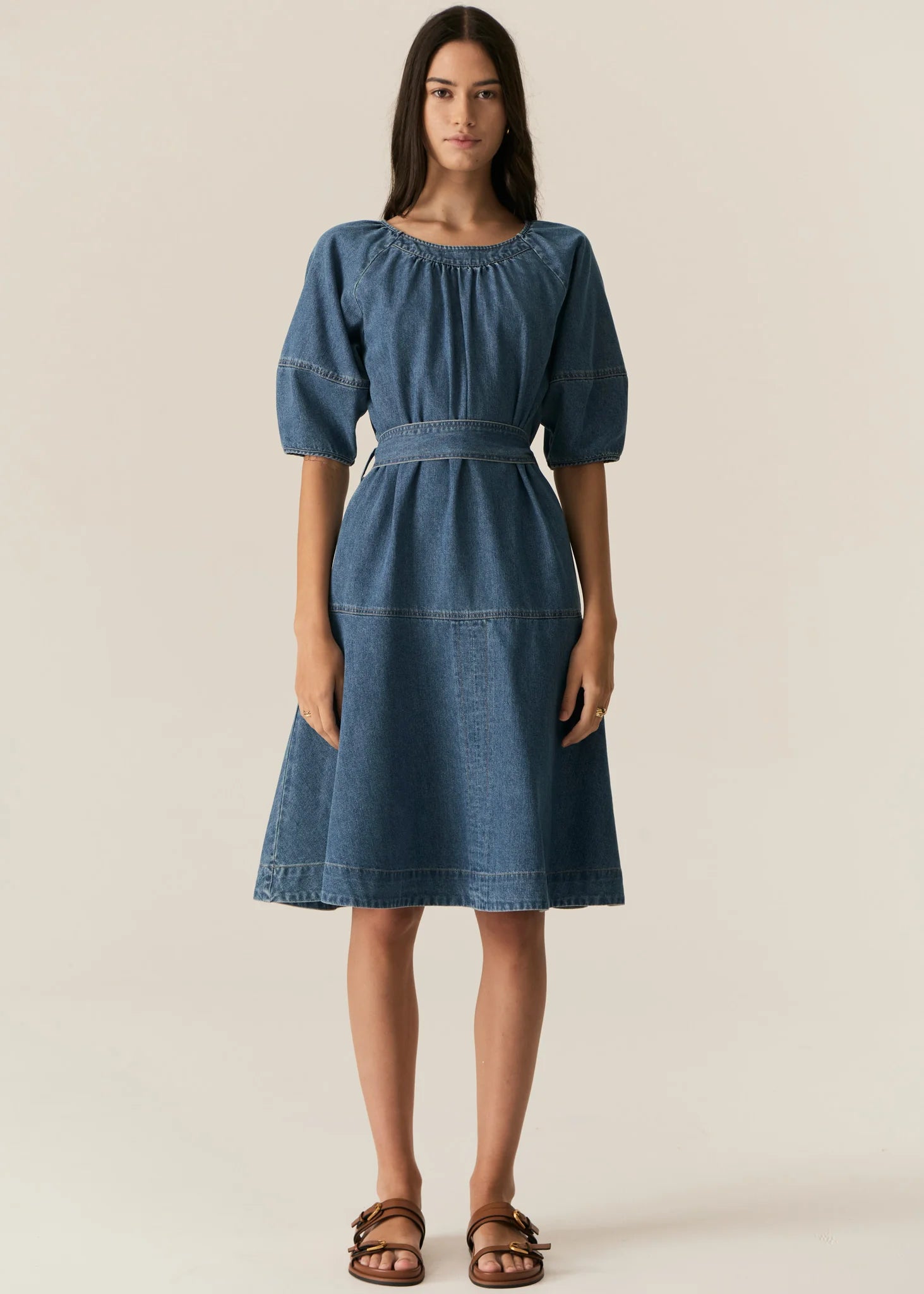 Woman wearing a blue denim short sleeve dress against a plain background