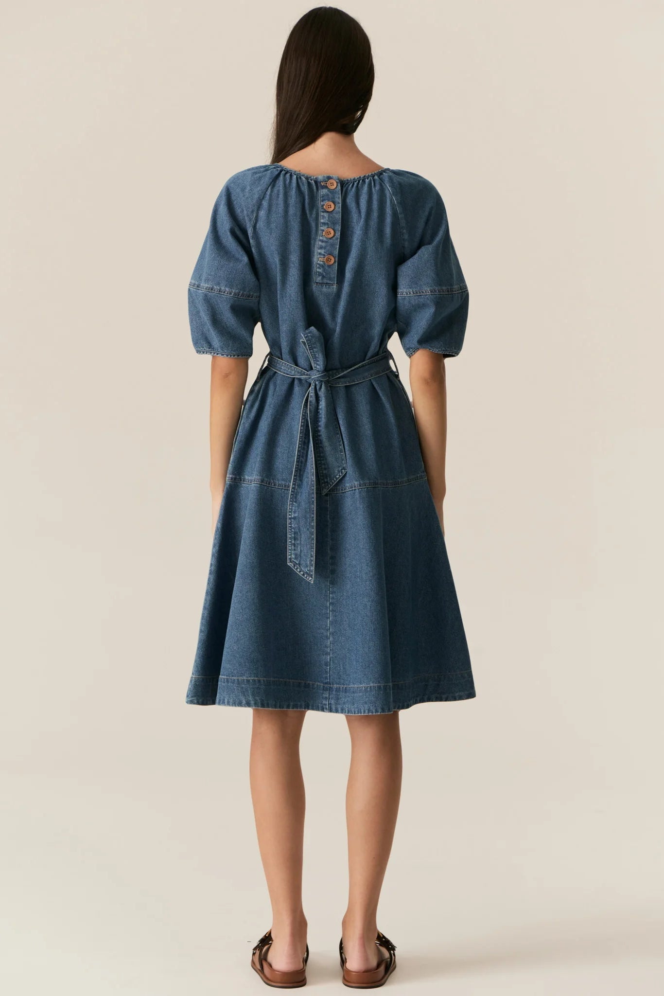 Woman wearing a blue denim short sleeve dress against a plain background