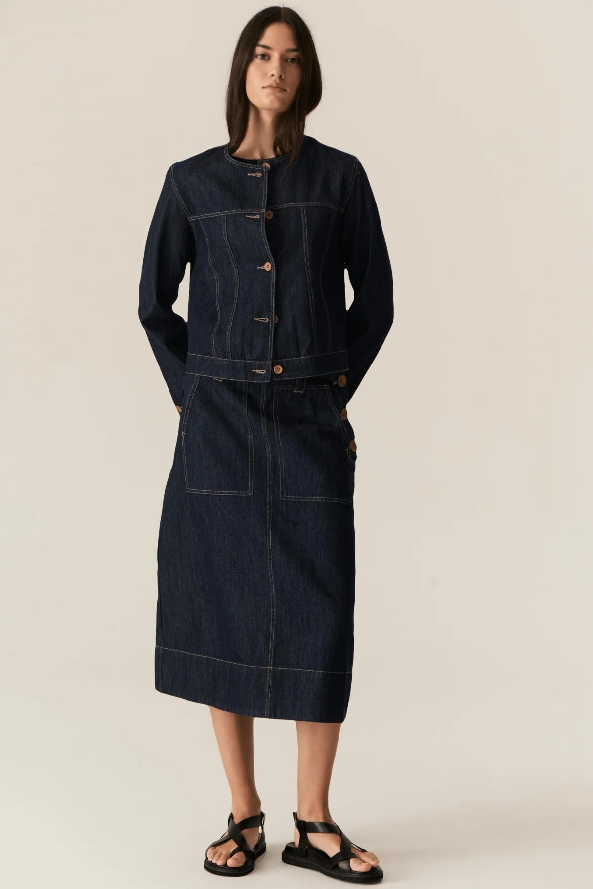 Woman wearing a dark denim jacket and skirt on a beige background