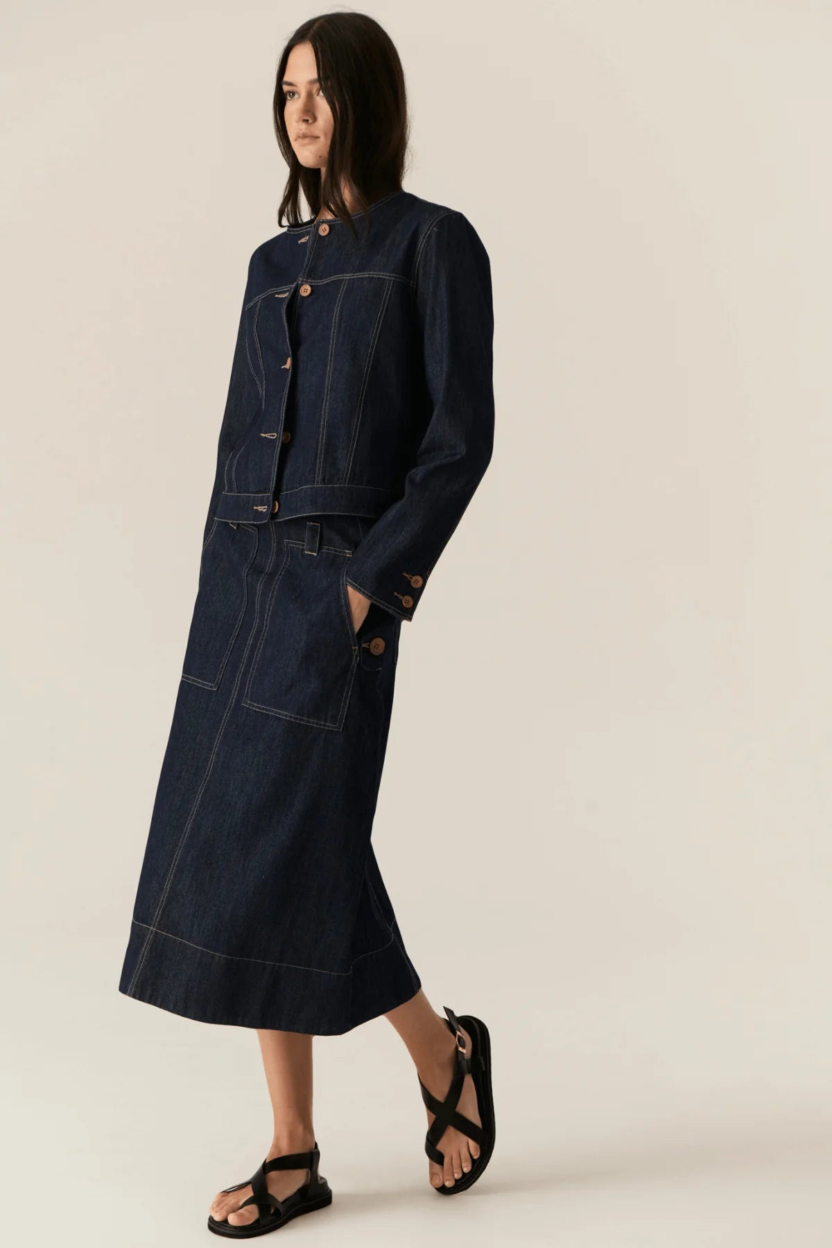 Woman wearing a dark denim jacket and skirt on a beige background