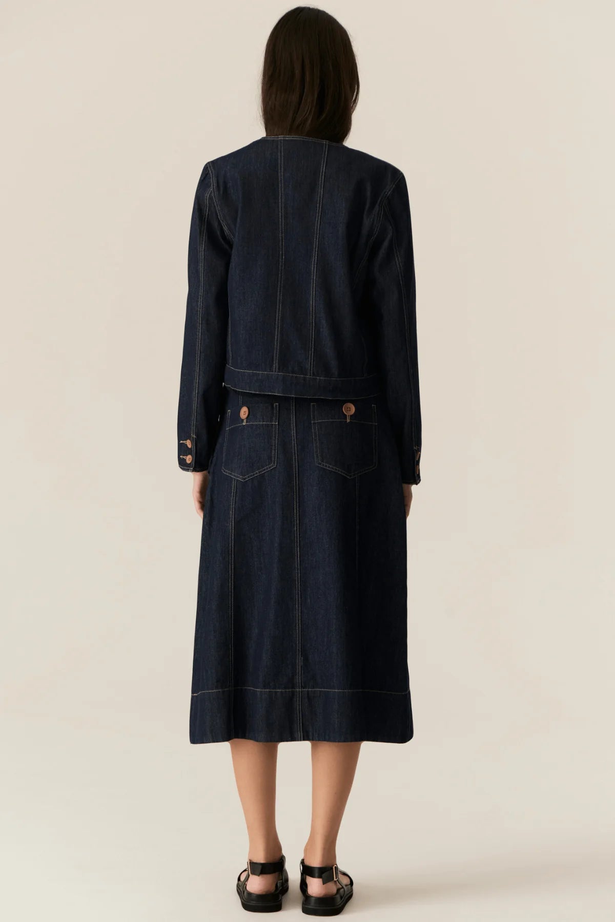Person wearing a dark denim jacket and skirt set on a beige background