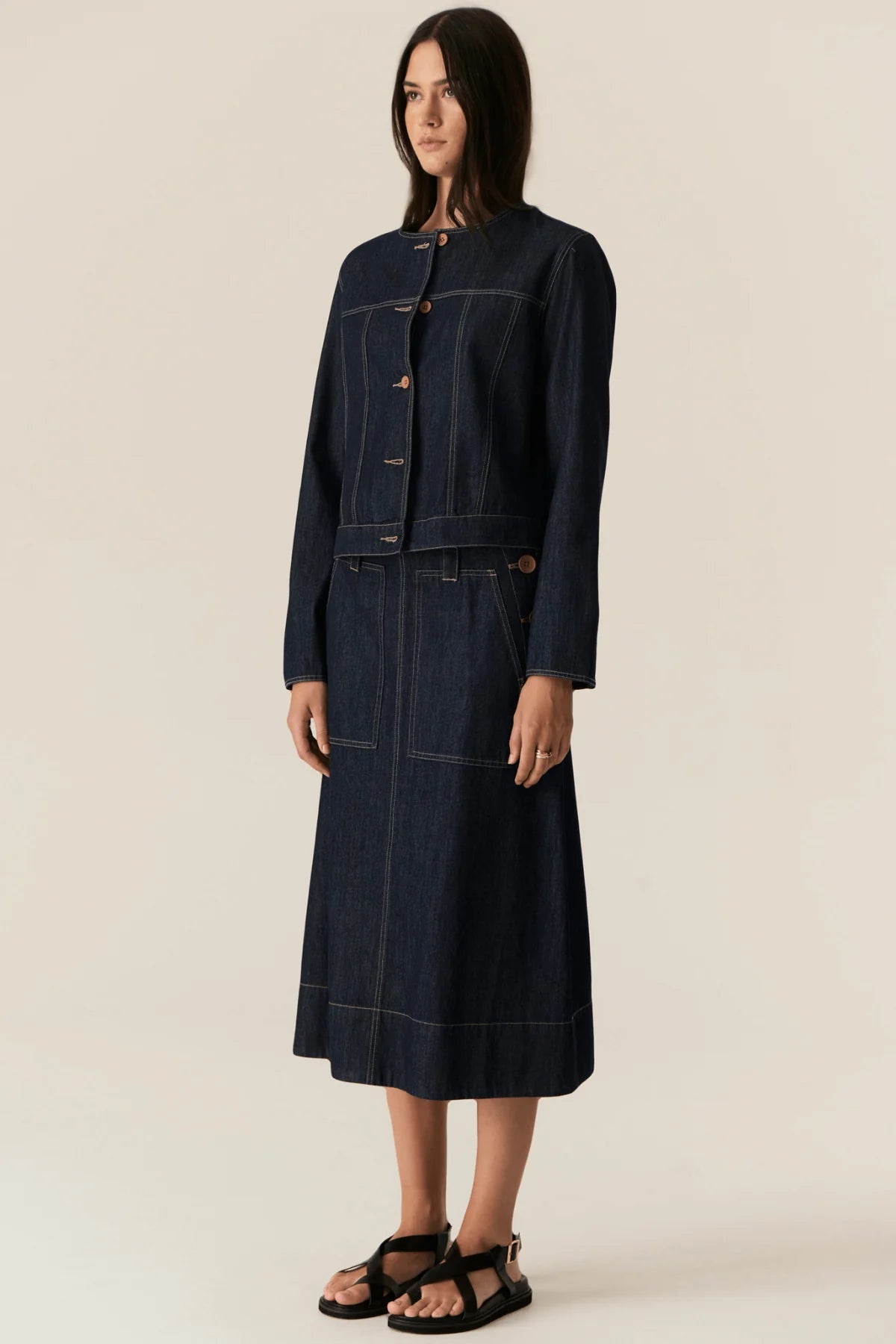 Woman wearing a dark denim jacket and skirt set on a beige background