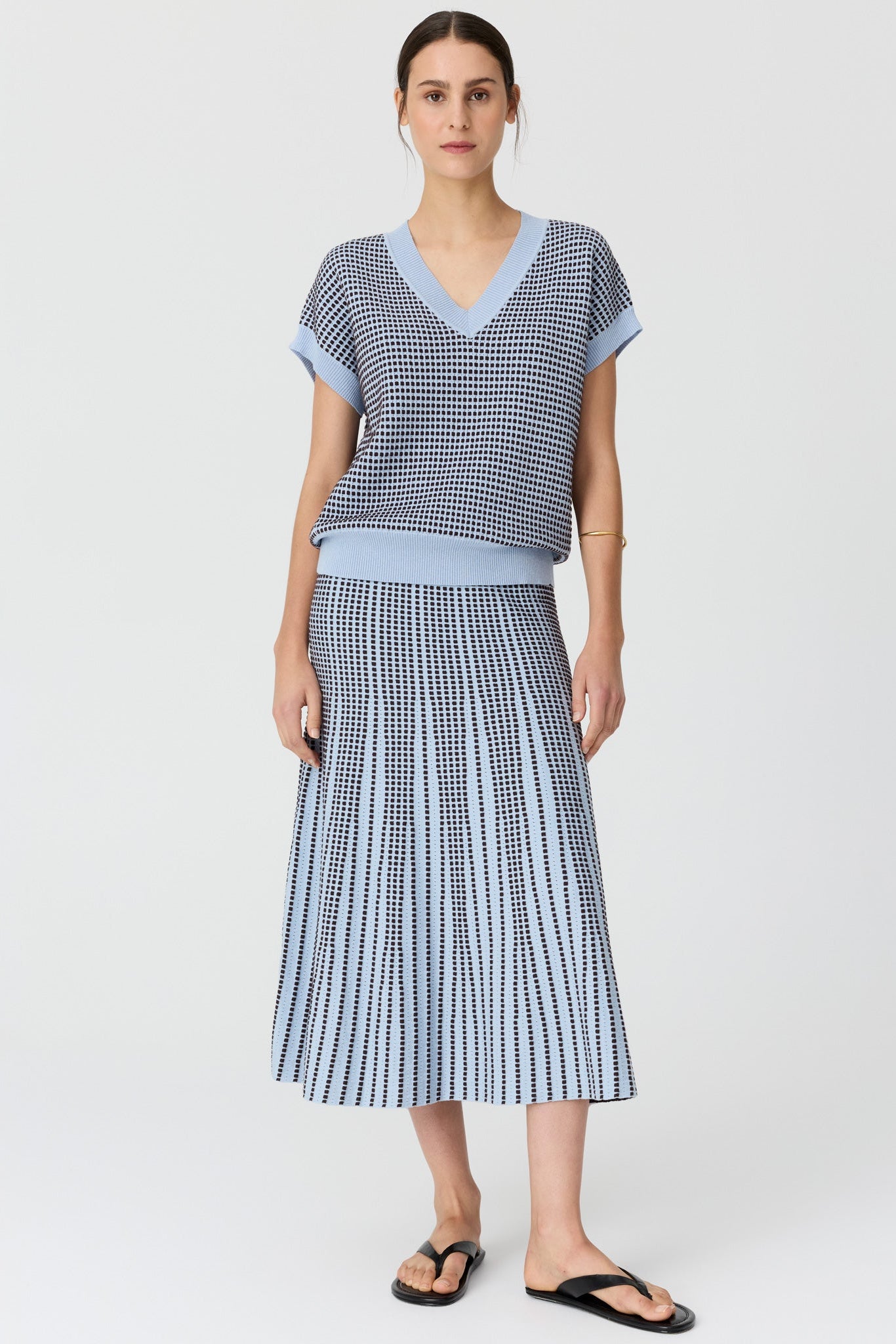 Women wearing a v neck short sleeve knit top in blue and chocolate pattern with a matching skirt and black sandals on a grey studio background. 