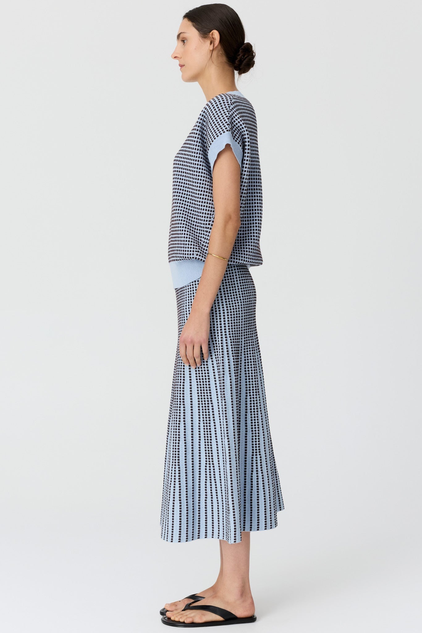 Women shown from the side wearing a v neck short sleeve knit top in blue and chocolate pattern with a matching skirt and black sandals on a grey studio background. 