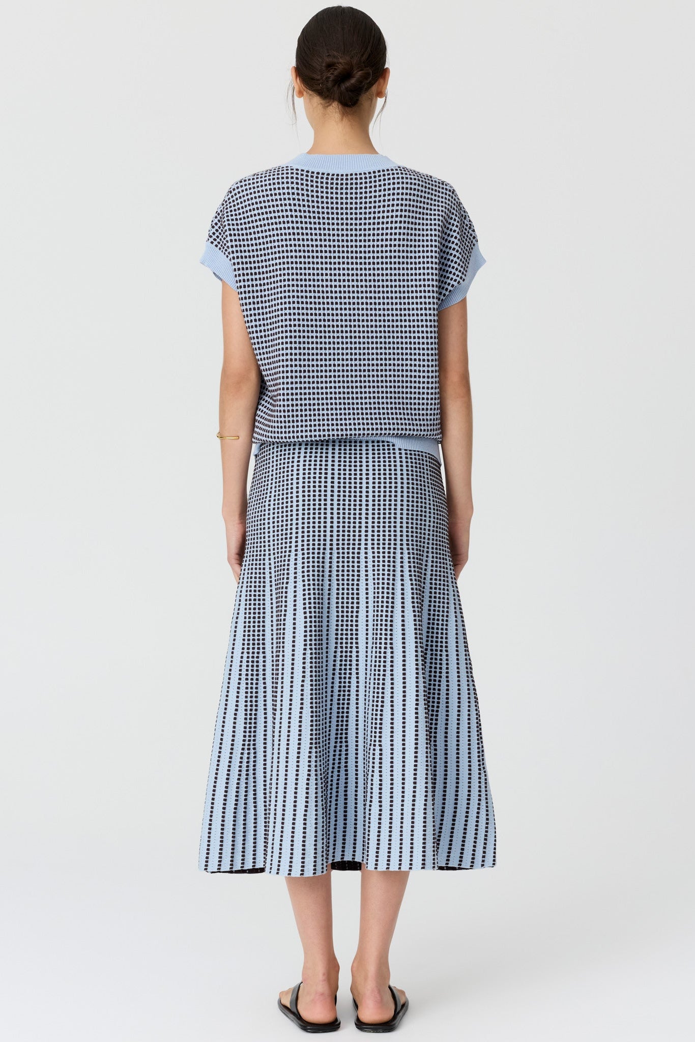 Women shown from the back wearing a v neck short sleeve knit top in blue and chocolate pattern with a matching skirt and black sandals on a grey studio background. 