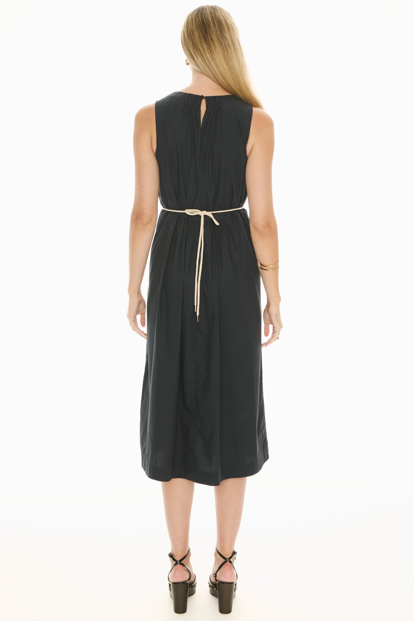 Model wearing a ink blue sleeveless midi dress with gathered waist  showing the back of the dress and tie and the waist on a white background